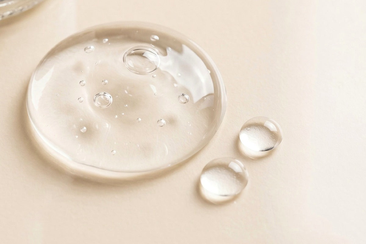 Clear gel serum texture with water droplets on a warm beige surface