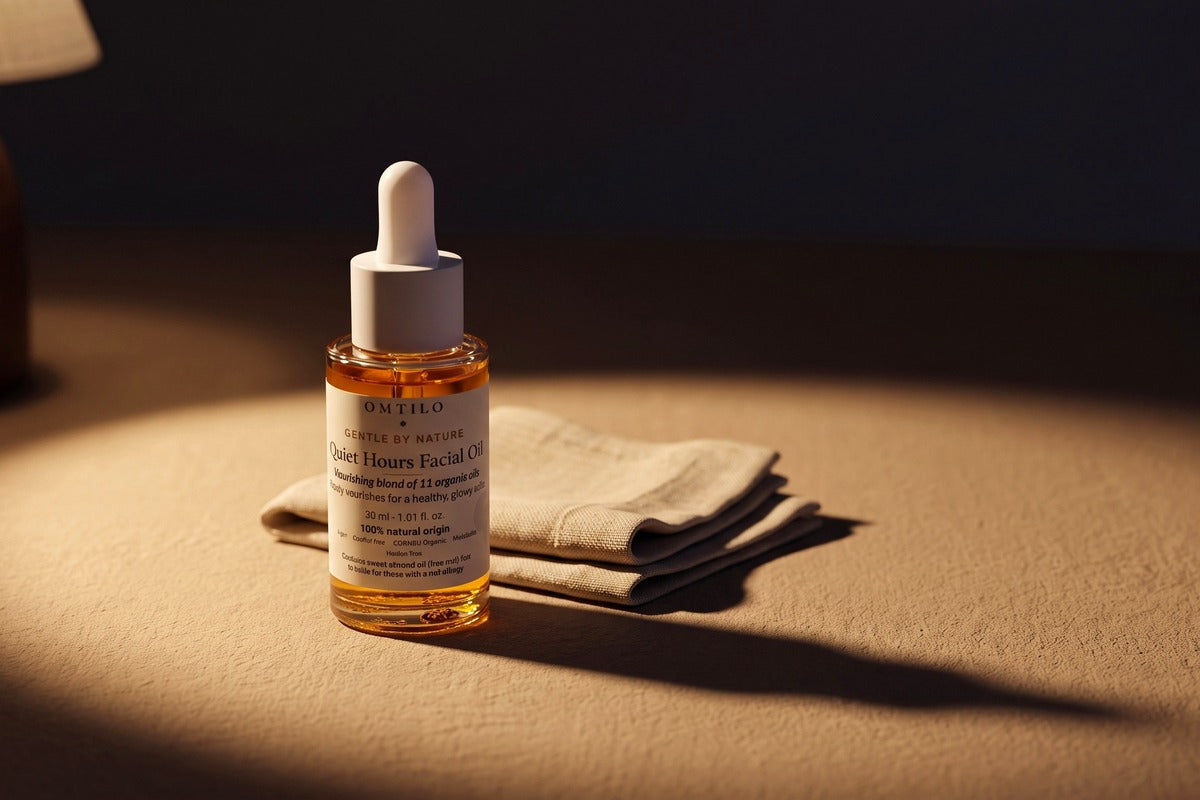 The OMTILO Quiet Hours Facial Oil in a pool of warm lamplight beside folded linen