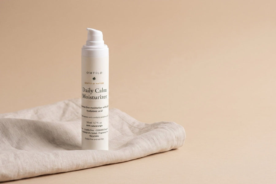 The OMTILO Daily Calm Moisturizer on clean folded linen, fragrance-free, on a warm beige background