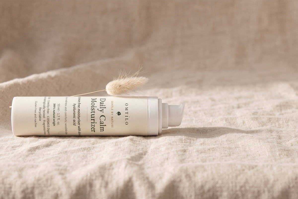 The OMTILO Daily Calm Moisturizer resting on linen with a dried grass stem, a calm still life