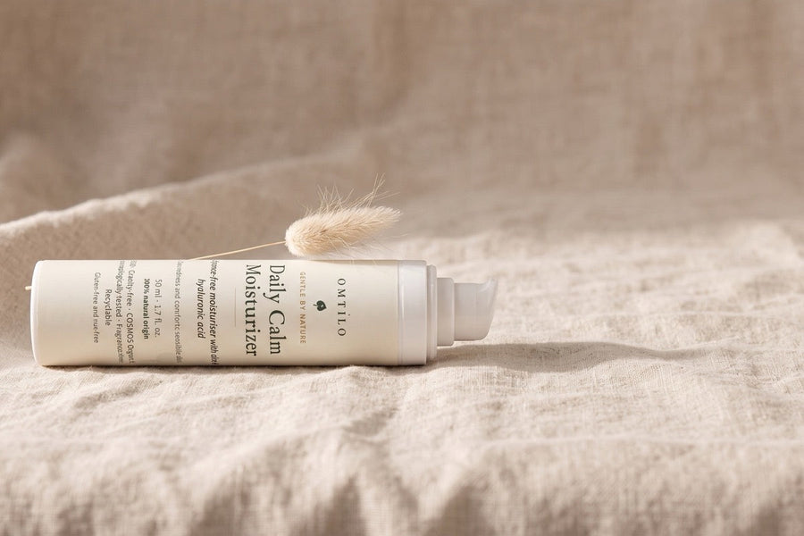 The OMTILO Daily Calm Moisturizer resting on linen with a dried grass stem, a calm still life